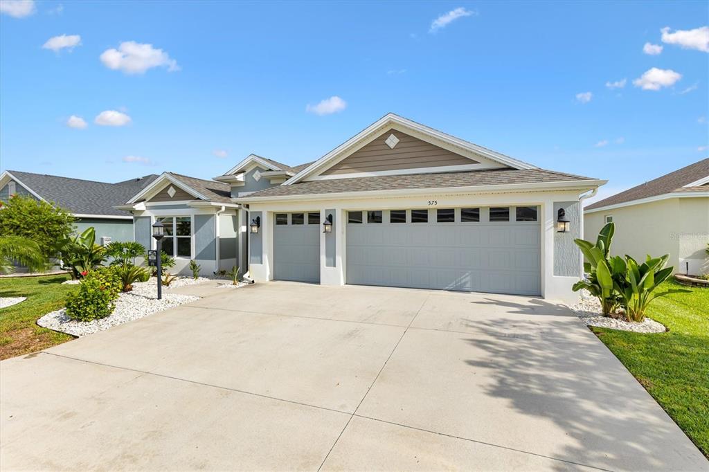 A suburban house exterior features a three-car garage, light blue siding, and a concrete driveway — 575 RANDALL ROAD, THE VILLAGES, FL