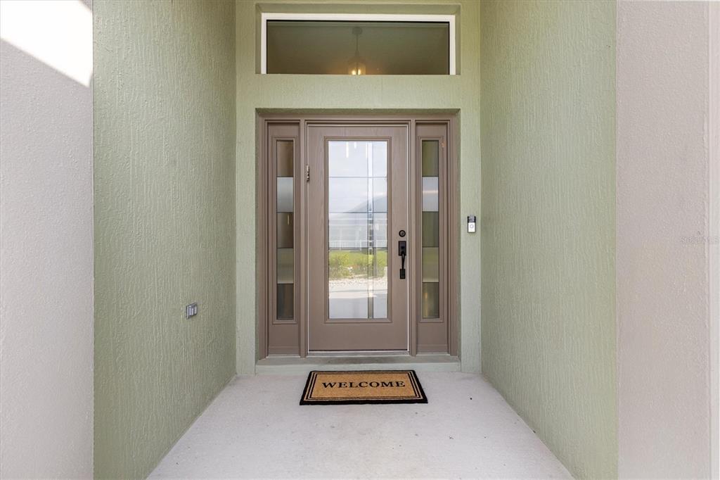 A front entryway features a tan door with glass panels and a welcome mat — 575 RANDALL ROAD, THE VILLAGES, FL