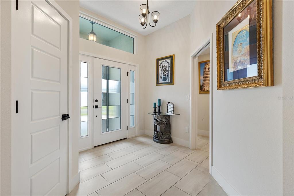 A bright entryway features white tile flooring, a glass-paneled front door, and framed wall art — 575 RANDALL ROAD, THE VILLAGES, FL