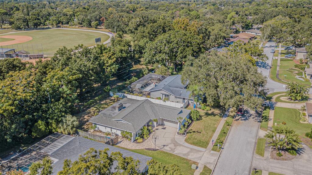 An aerial view of a suburban house with a driveway, pool cage, and nearby baseball field — 565 SANDY HOOK ROAD, PALM HARBOR, FL
