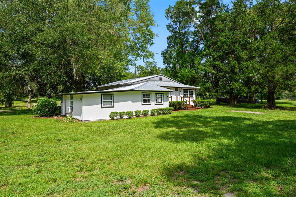 A white single-story house with a metal roof sits on a large, grassy lot — 6218 SW 202ND STREET, NEWBERRY, FL