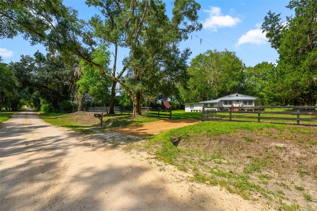A white house sits behind a wooden fence on a dirt road with large trees — 6218 SW 202ND STREET, NEWBERRY, FL