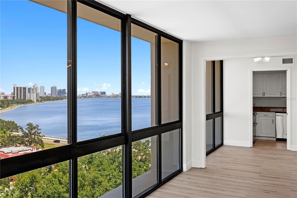 A room with floor-to-ceiling windows overlooking a bay and city skyline, adjacent to a kitchen — 3301 BAYSHORE BOULEVARD UNIT 1101E, TAMPA, FL