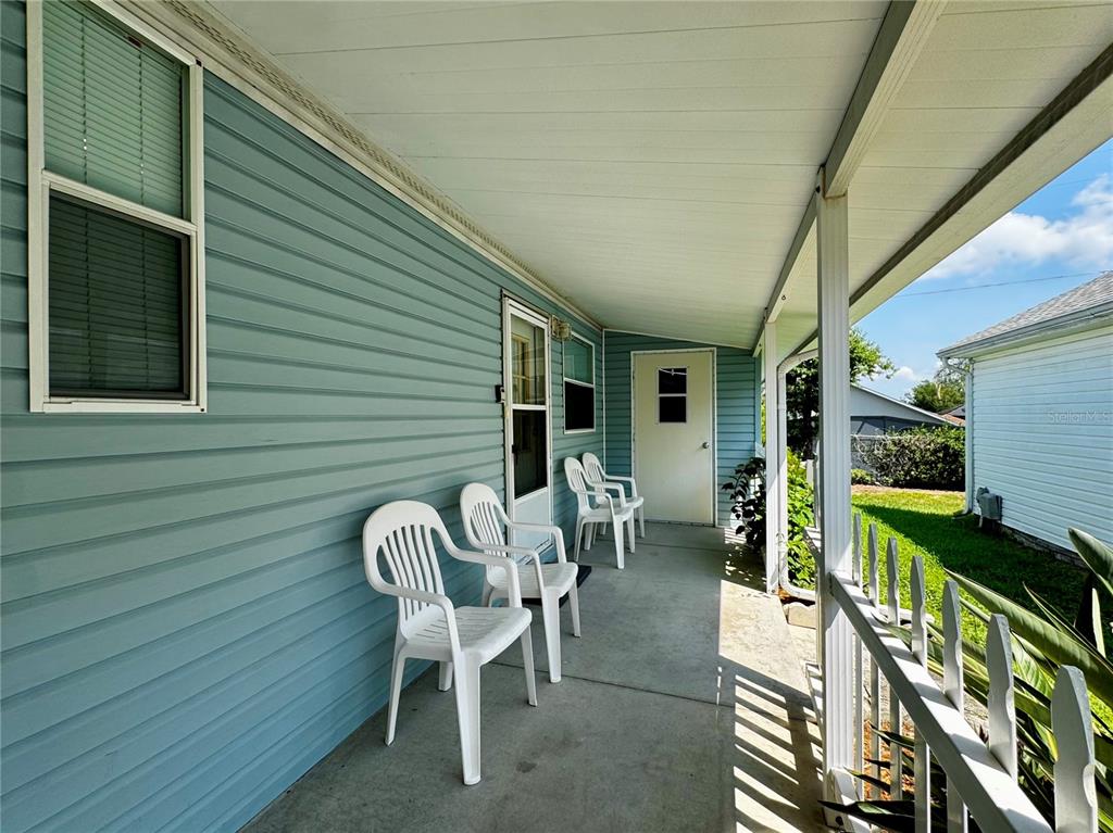 A covered porch with light blue siding, white plastic chairs, and a white picket railing — 50989 HIGHWAY 27 UNIT 182, DAVENPORT, FL