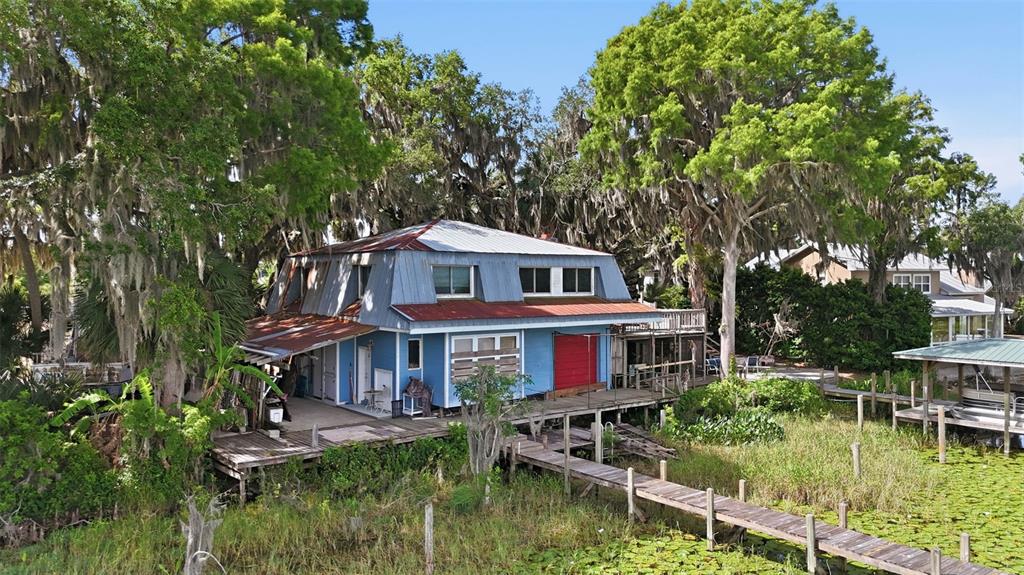 A blue two-story house with a metal roof sits on a wooden dock over water — 400 LAKESHORE DRIVE, EUSTIS, FL