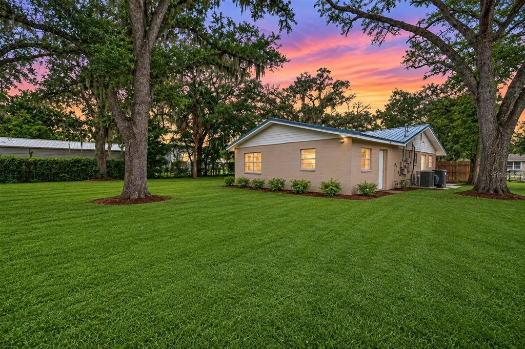 A tan brick house with a metal roof sits on a large, grassy lawn with trees — 205 2ND AVENUE SE, RUSKIN, FL