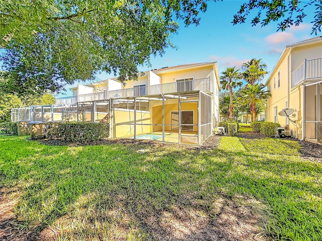A two-story townhouse with a screened-in patio and pool viewed from the grassy backyard — 17508 BLESSING DRIVE, CLERMONT, FL