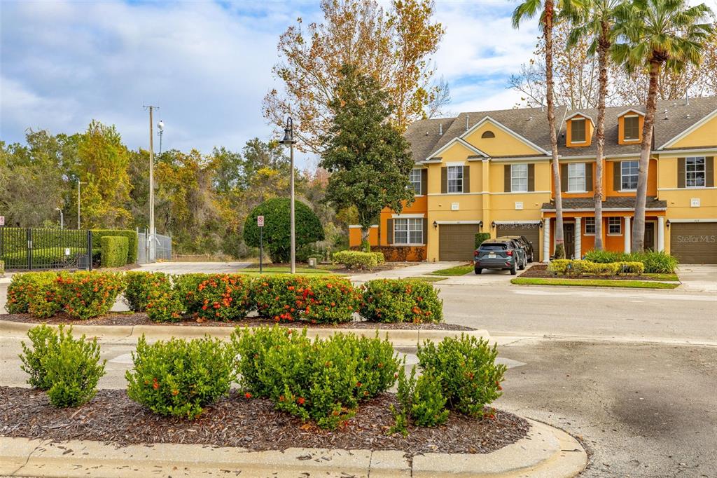 A view of a yellow multi-story townhouse complex with a parking area and landscaping — 811 ASSEMBLY COURT, REUNION, FL