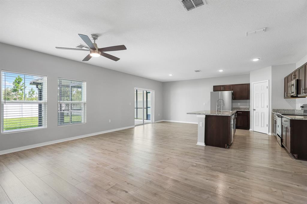 An open-concept kitchen and living area features light wood-look flooring and dark wood cabinetry — 12894 FRENCH MARKET DRIVE, RIVERVIEW, FL