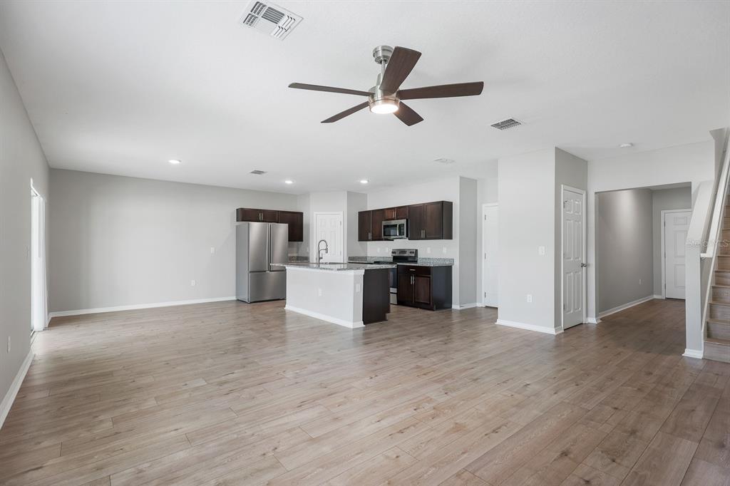 An open-concept kitchen and living area featuring wood-look flooring, dark cabinetry, and a center island — 12894 FRENCH MARKET DRIVE, RIVERVIEW, FL