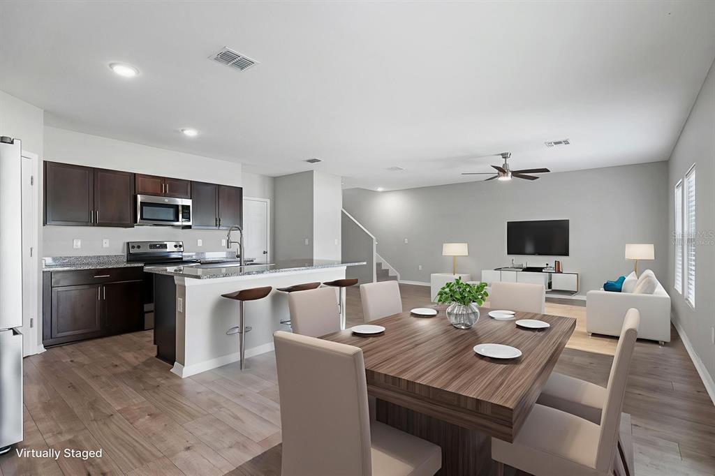 A kitchen with dark cabinets and an island opens to a dining area and living room — 12894 FRENCH MARKET DRIVE, RIVERVIEW, FL
