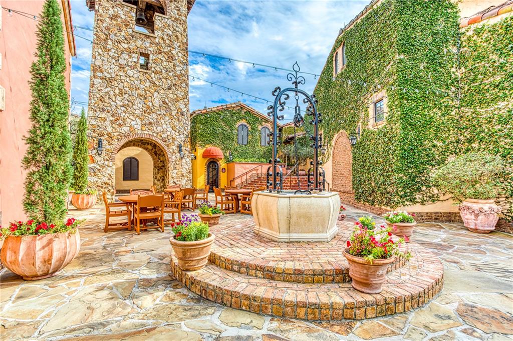 A stone courtyard features a central well, patio furniture, and buildings covered in ivy — 16748 ARTIMINO LOOP, MONTVERDE, FL