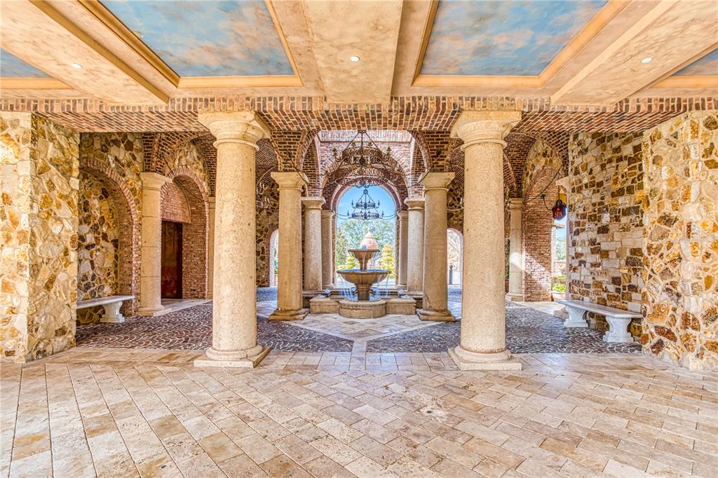 A stone-walled outdoor courtyard features a central fountain, arched brick ceilings, and classical columns — 16748 ARTIMINO LOOP, MONTVERDE, FL