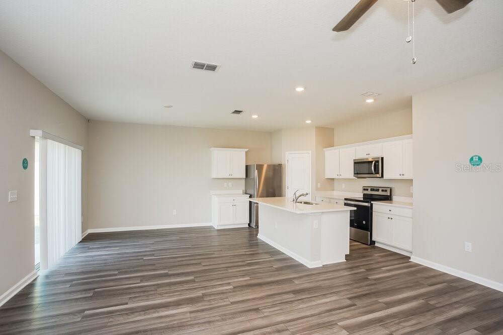 An open-concept kitchen and living area featuring white cabinetry, stainless appliances, and wood-look flooring — 912 KELLY FERN LOOP, RUSKIN, FL
