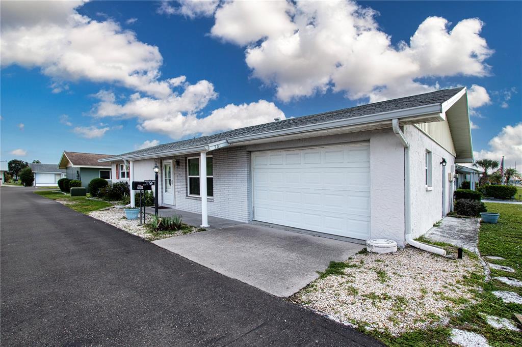 A light-colored single-story house features a white garage door and a small front porch — 701 READING PLACE, SUN CITY CENTER, FL