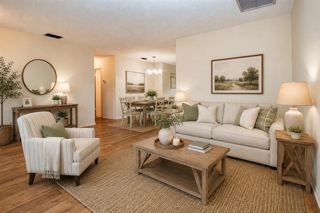 A living room with light wood floors, a beige sofa, an armchair, and a dining area — 701 READING PLACE, SUN CITY CENTER, FL