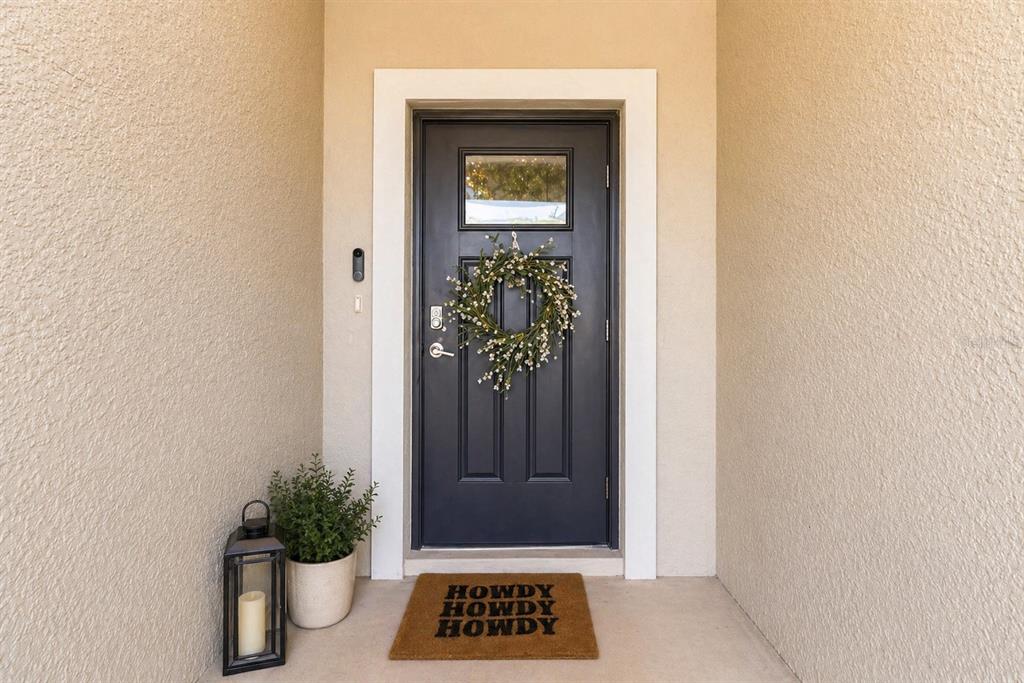 A dark gray front door with a wreath and a welcome mat sits in a recessed entryway — 2549 SUNRAY VENUS WAY, RUSKIN, FL