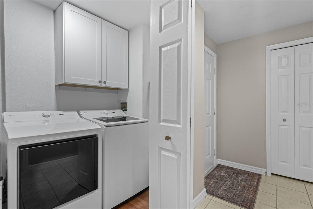 A laundry room features white appliances, upper cabinets, and tiled flooring — 6663 QUEENS BOROUGH AVENUE UNIT 104, ORLANDO, FL