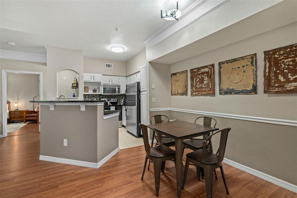 A dining area with a wooden table and chairs sits adjacent to a kitchen — 6663 QUEENS BOROUGH AVENUE UNIT 104, ORLANDO, FL