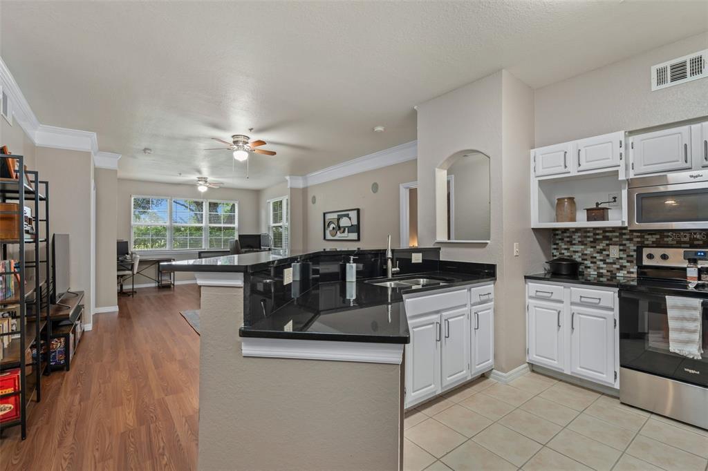 A kitchen with white cabinets and black countertops overlooks a living area with wood flooring — 6663 QUEENS BOROUGH AVENUE UNIT 104, ORLANDO, FL
