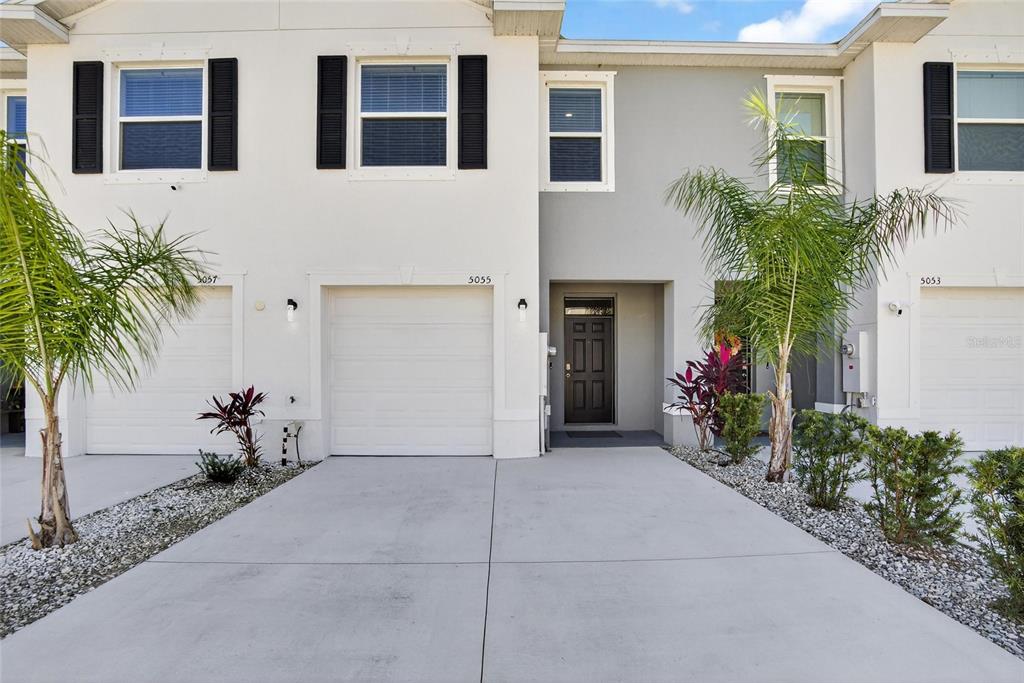 A two-story townhouse exterior features a white garage, a dark front door, and palm trees — 5055 CAPTAIN DAVIS DRIVE, WIMAUMA, FL