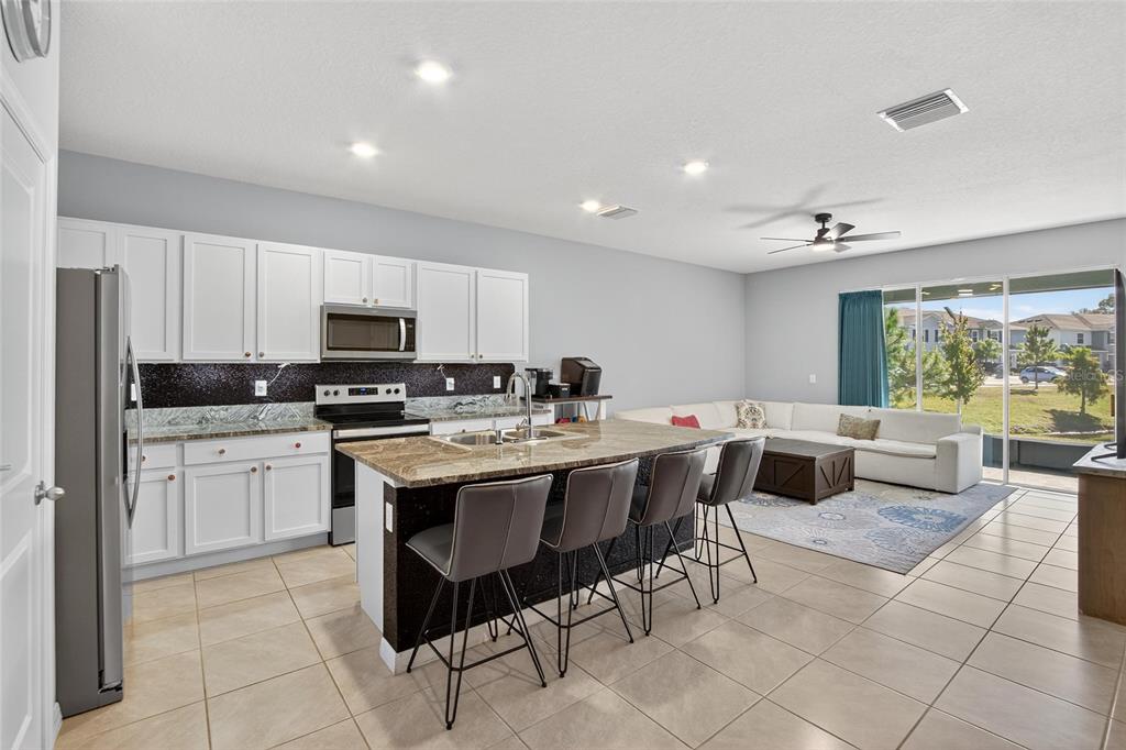An open-concept kitchen with white cabinets, granite countertops, and a breakfast bar faces a living area — 5055 CAPTAIN DAVIS DRIVE, WIMAUMA, FL