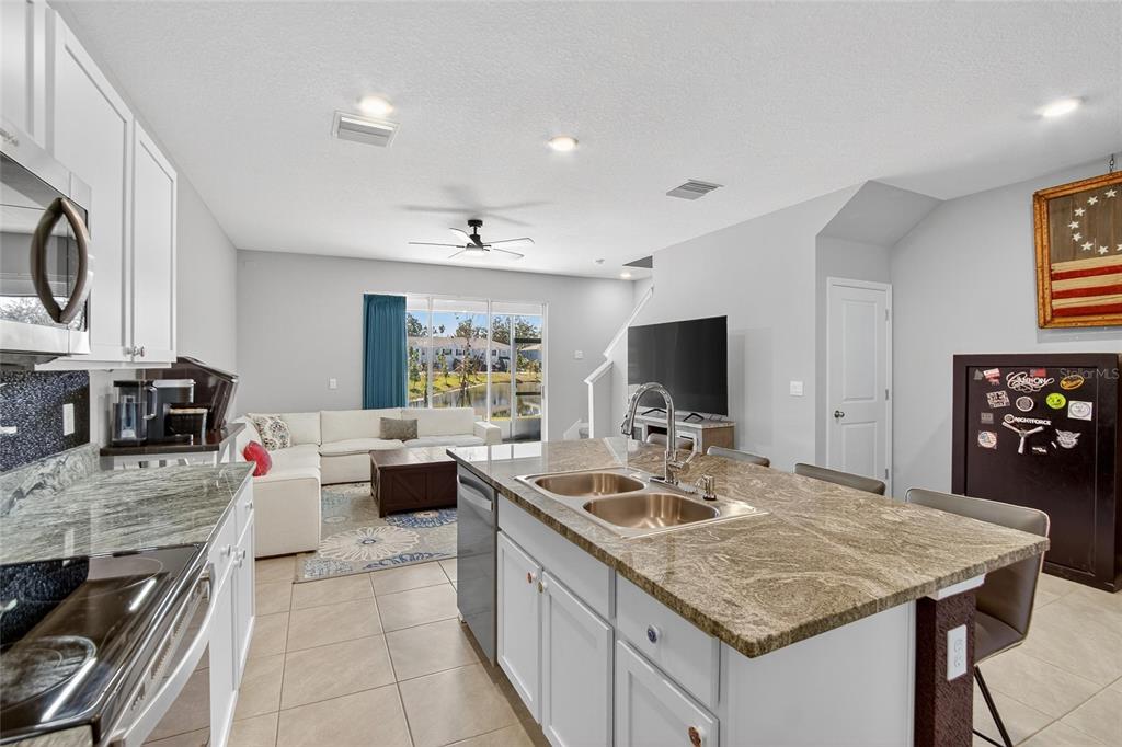 A modern kitchen with granite countertops and a central island overlooks an open-concept living area — 5055 CAPTAIN DAVIS DRIVE, WIMAUMA, FL