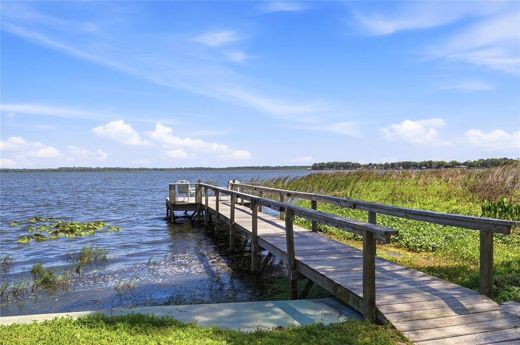 A boat dock with a metal roof sits on the grassy shore of a lake — 8342 W LAKE MARION ROAD, HAINES CITY, FL