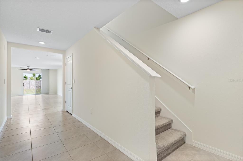 A hallway with tile flooring leads to a living area, with carpeted stairs on the right — 16555 MOSAIC OAR DRIVE, WIMAUMA, FL