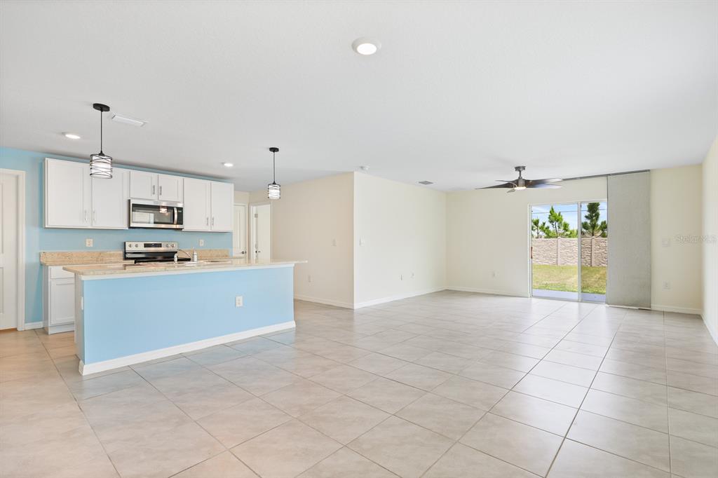 An open-concept kitchen with a blue island and white cabinets overlooks a tiled living area — 16555 MOSAIC OAR DRIVE, WIMAUMA, FL