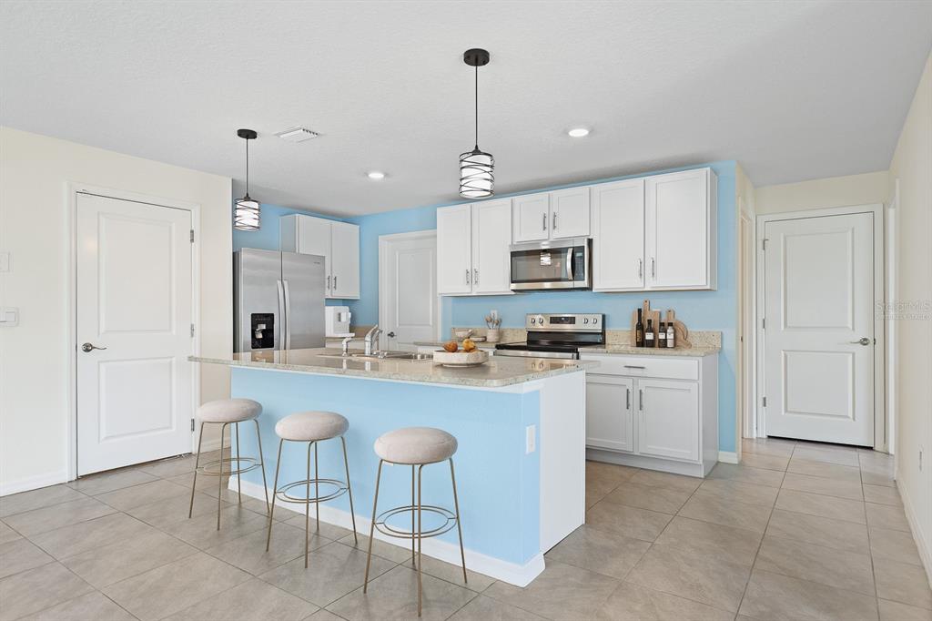 A kitchen features white cabinets, a light blue island with bar stools, and tile flooring — 16555 MOSAIC OAR DRIVE, WIMAUMA, FL