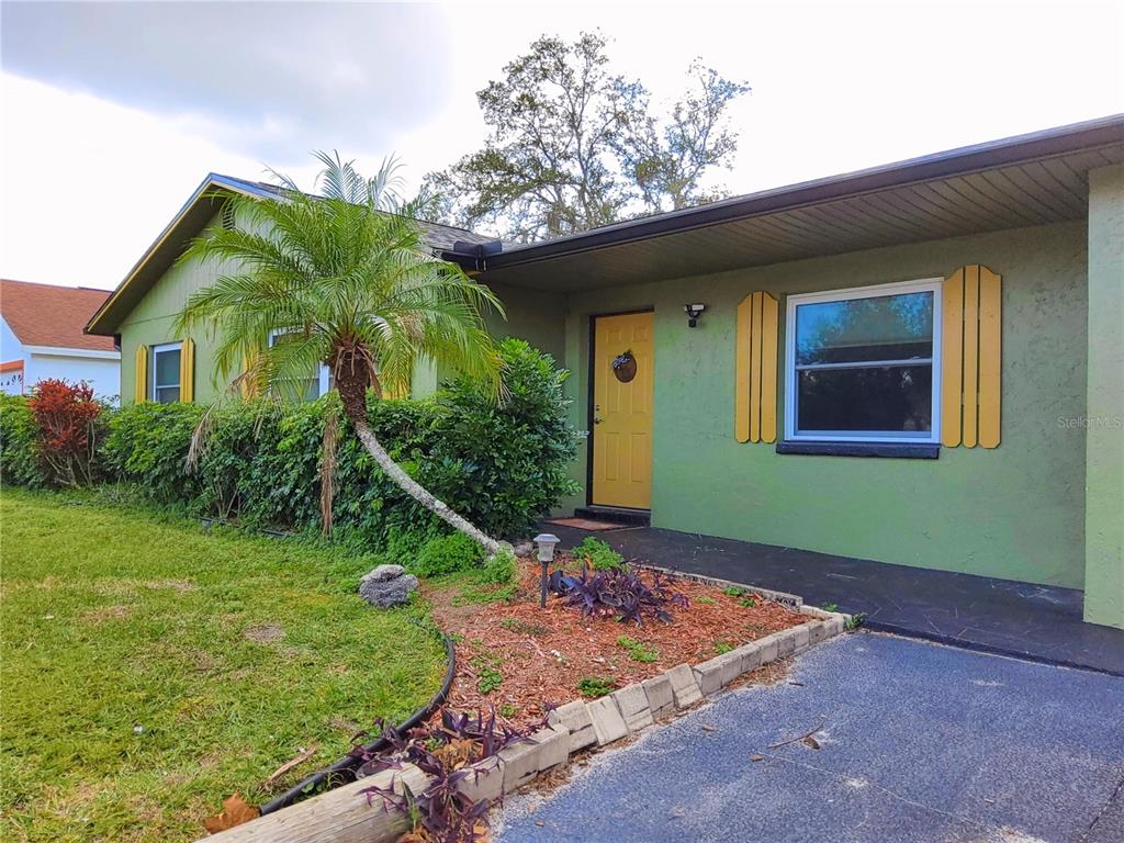 A green house exterior features a yellow front door, palm tree, and paved driveway — 4297 CANELA ROAD, COCOA, FL