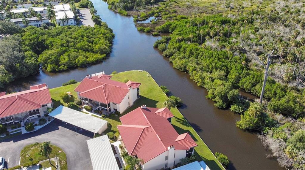 An aerial view shows multi-story buildings with red roofs situated beside a winding river — 9940 EAGLES POINT CIRCLE UNIT 4, PORT RICHEY, FL