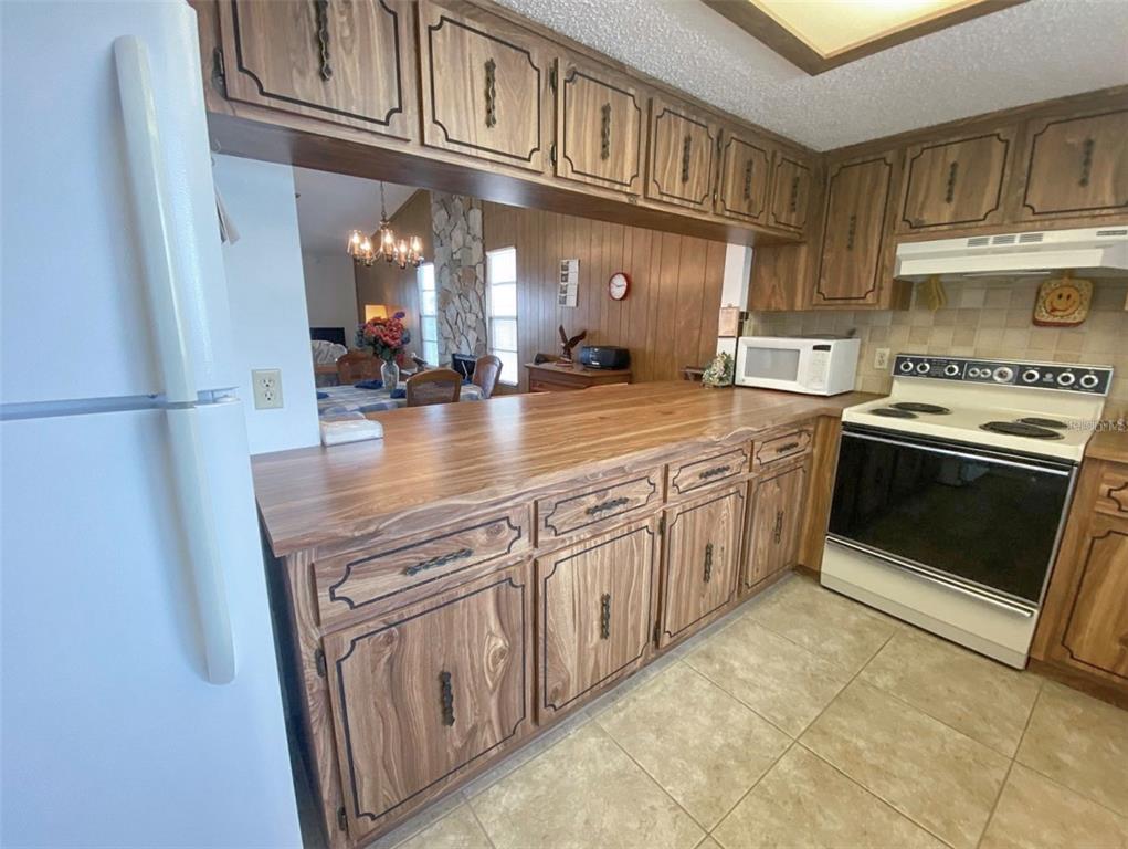 A kitchen features wood-grain cabinets, a laminate countertop, and a view into the dining area — 9940 EAGLES POINT CIRCLE UNIT 4, PORT RICHEY, FL
