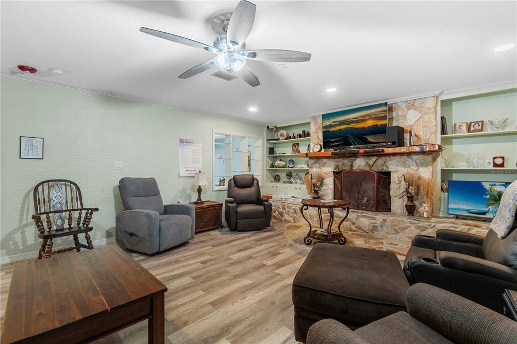 A living room features a stone fireplace, wood-look flooring, a ceiling fan, and built-in shelving — 207 W WHEELER ROAD, SEFFNER, FL