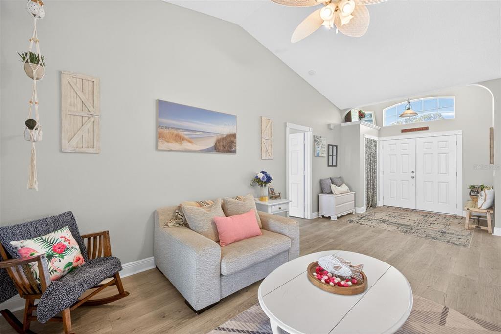 A living room features light wood flooring, a vaulted ceiling, a sofa, and an entryway — 3907 57TH PLACE E, BRADENTON, FL