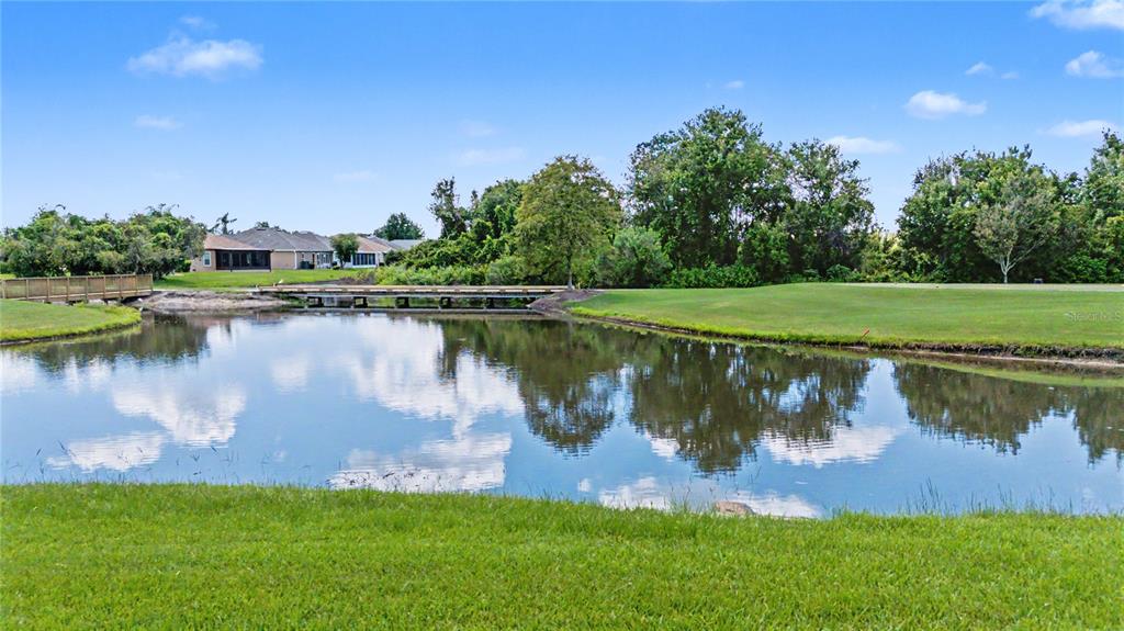 A pond reflects the sky and a wooden footbridge in front of suburban houses — 10231 CLEGHORN DRIVE, SAN ANTONIO, FL