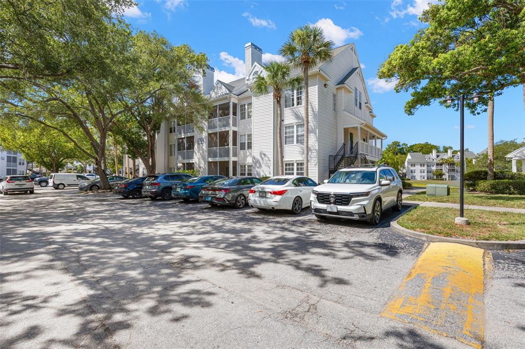 A multi-story apartment building with screened balconies sits next to a paved parking lot — 3310 HAVILAND COURT UNIT 104, PALM HARBOR, FL