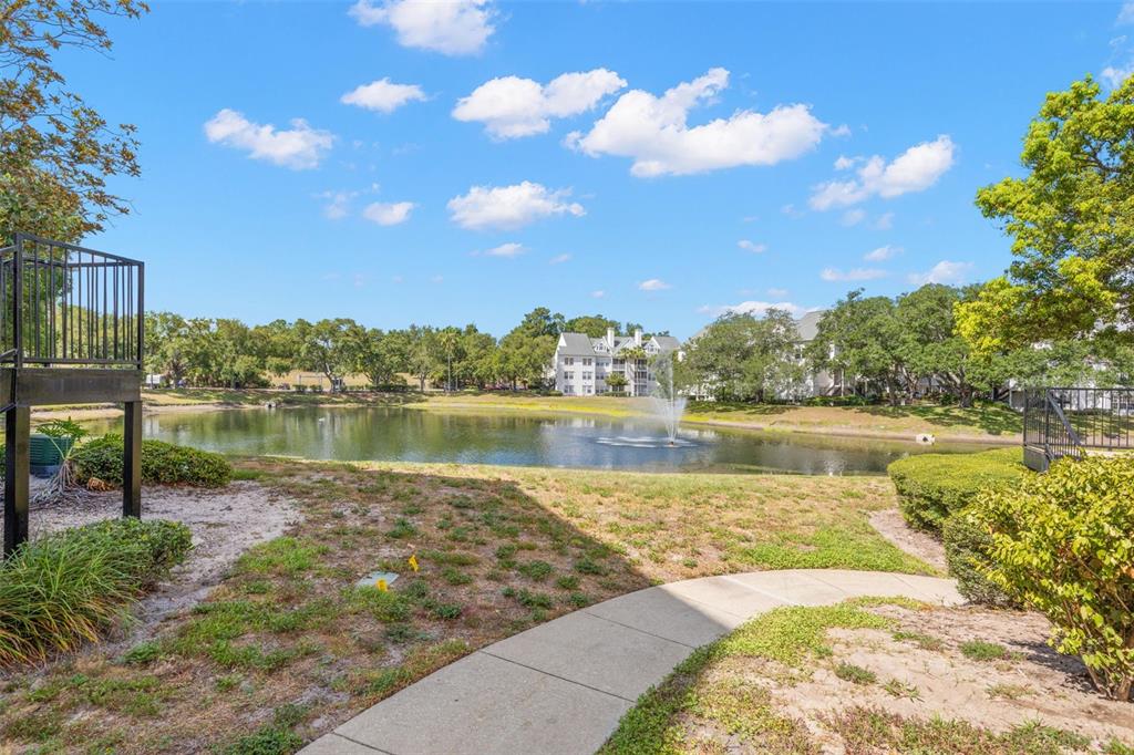 The exterior of a multi-story apartment building features a walkway, stairs, and a pond — 3310 HAVILAND COURT UNIT 104, PALM HARBOR, FL