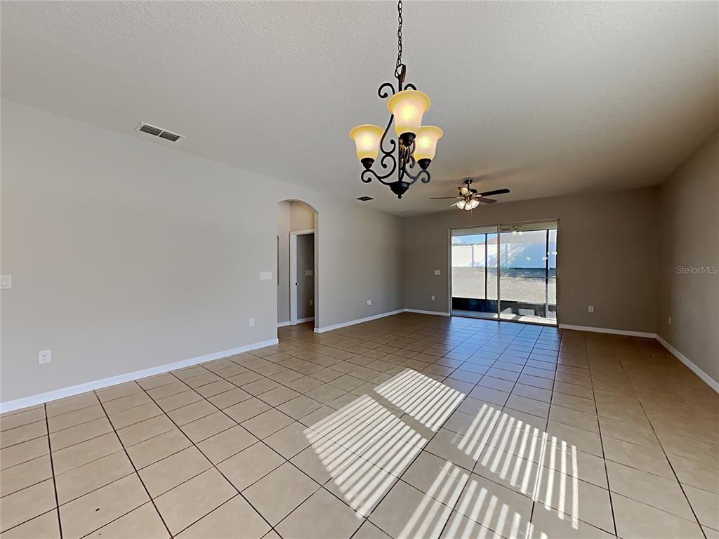 An open-concept living area features beige tile flooring, a chandelier, and sliding glass doors — 1328 ARONIMINIK DRIVE, MOUNT DORA, FL