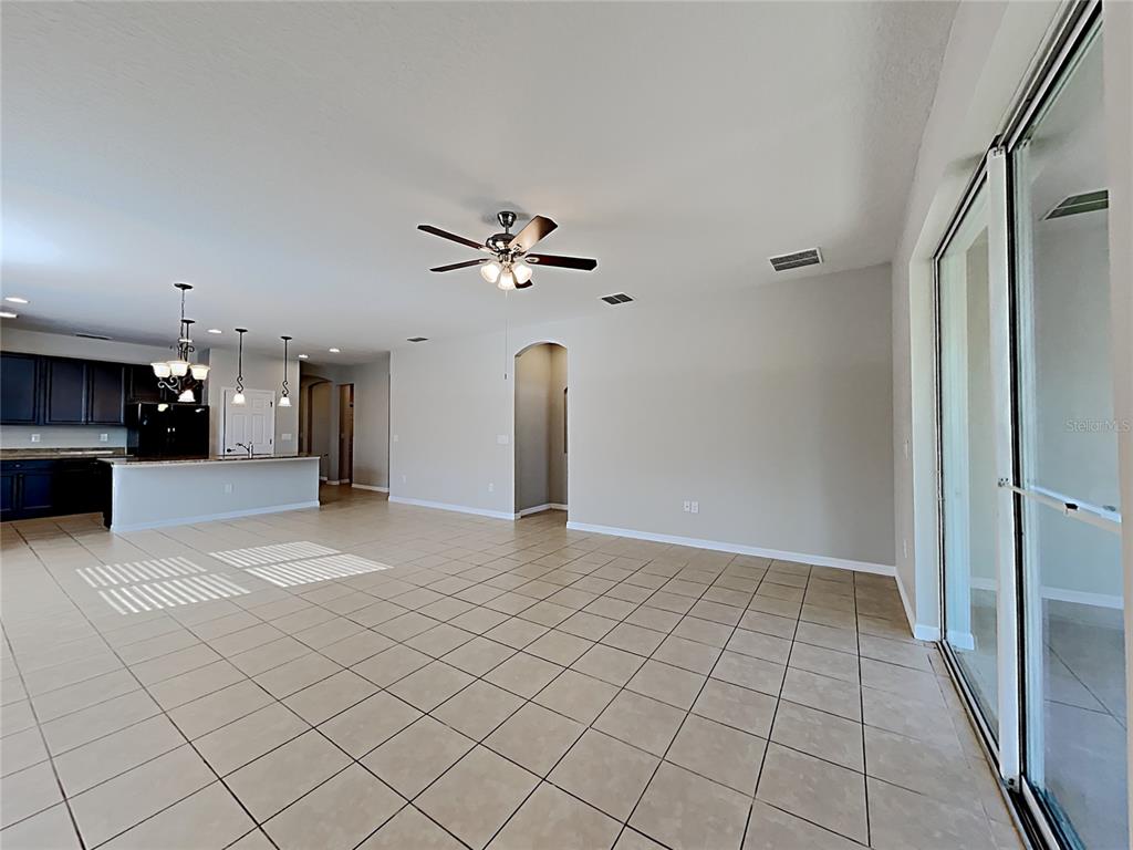An open-concept living area features tile flooring, a ceiling fan, and an adjacent kitchen — 1328 ARONIMINIK DRIVE, MOUNT DORA, FL