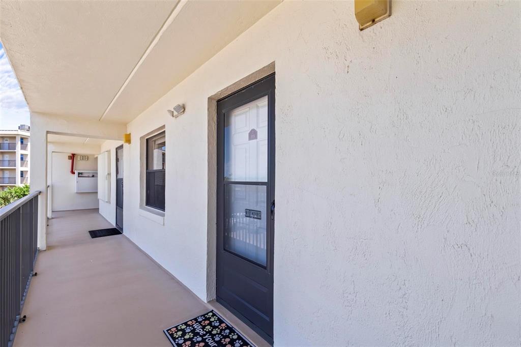 An exterior hallway features a dark-framed screen door, a doormat, and a metal railing — 2700 OCEAN SHORE BOULEVARD UNIT 315, ORMOND BEACH, FL