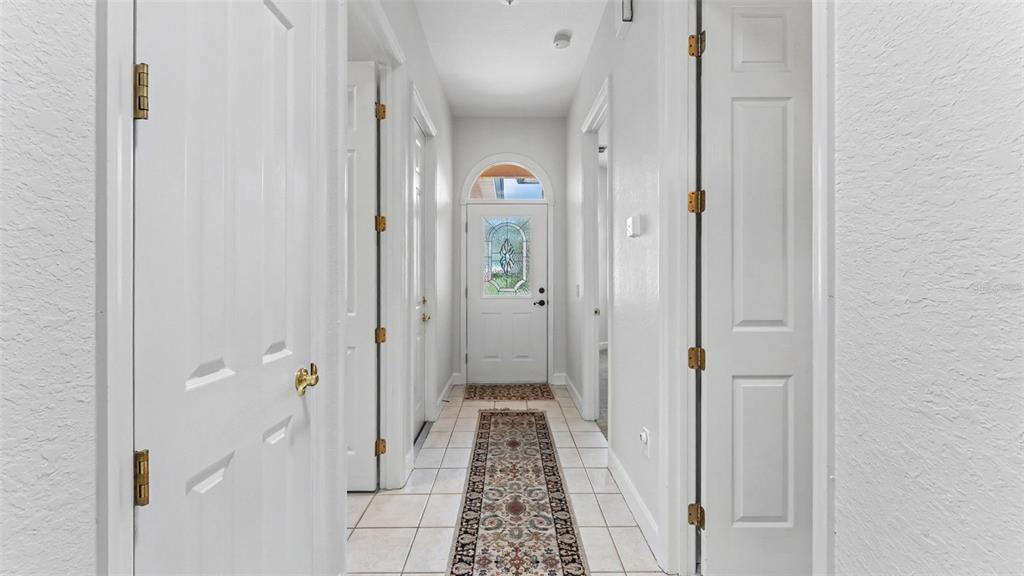 A hallway with white doors, tiled floors, a patterned runner rug, and a glass-paneled front door — 1230 MOTORCOACH DRIVE, POLK CITY, FL