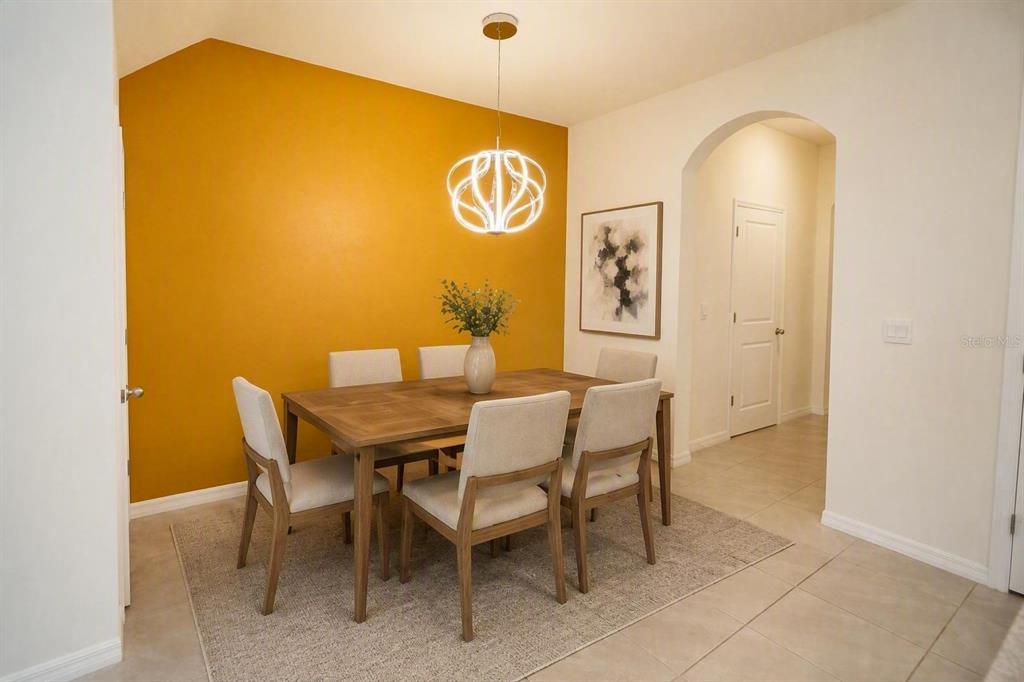 A dining room features a mustard yellow accent wall, a wooden table, and modern lighting — 34347 SORREL MINT DRIVE, WESLEY CHAPEL, FL