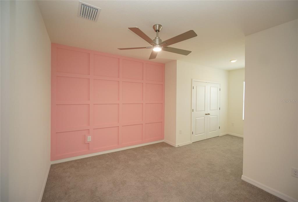 A bedroom features a pink grid-paneled accent wall, gray carpeting, and a ceiling fan — 34347 SORREL MINT DRIVE, WESLEY CHAPEL, FL