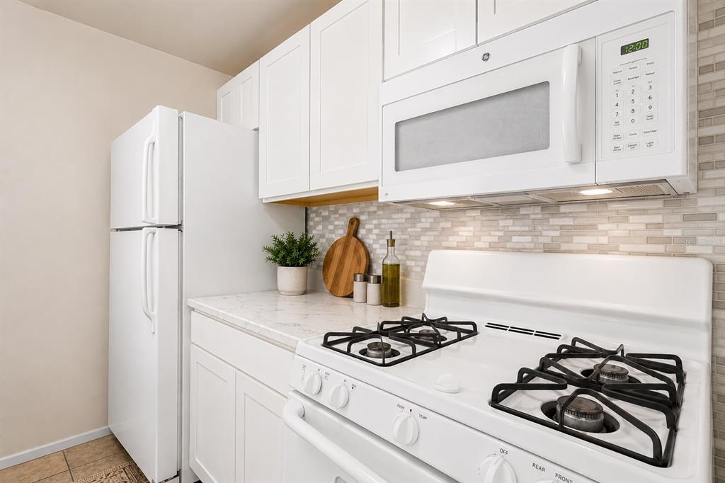 A kitchen features white cabinets, a white refrigerator, a gas stove, and a tiled backsplash — 2035 DIXIE BELLE DRIVE UNIT 2035M, ORLANDO, FL