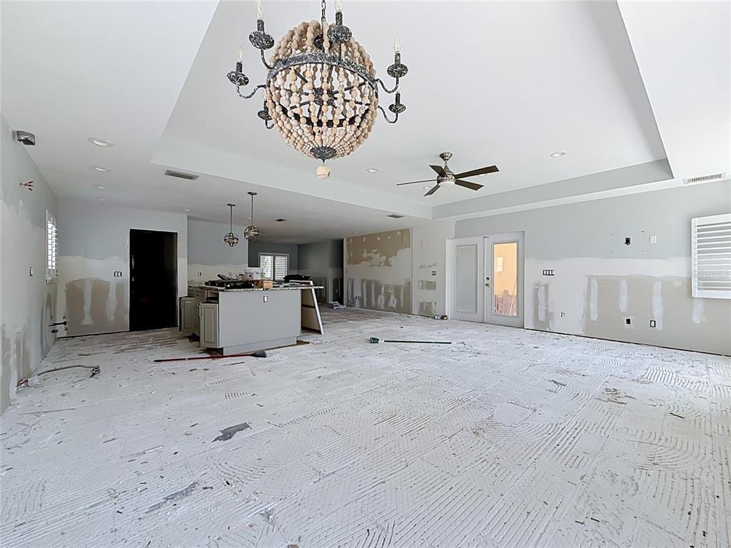 An unfinished living room and kitchen area features a beaded chandelier, ceiling fan, and bare floors — 2010 BAYOU GRANDE BOULEVARD NE, ST PETERSBURG, FL