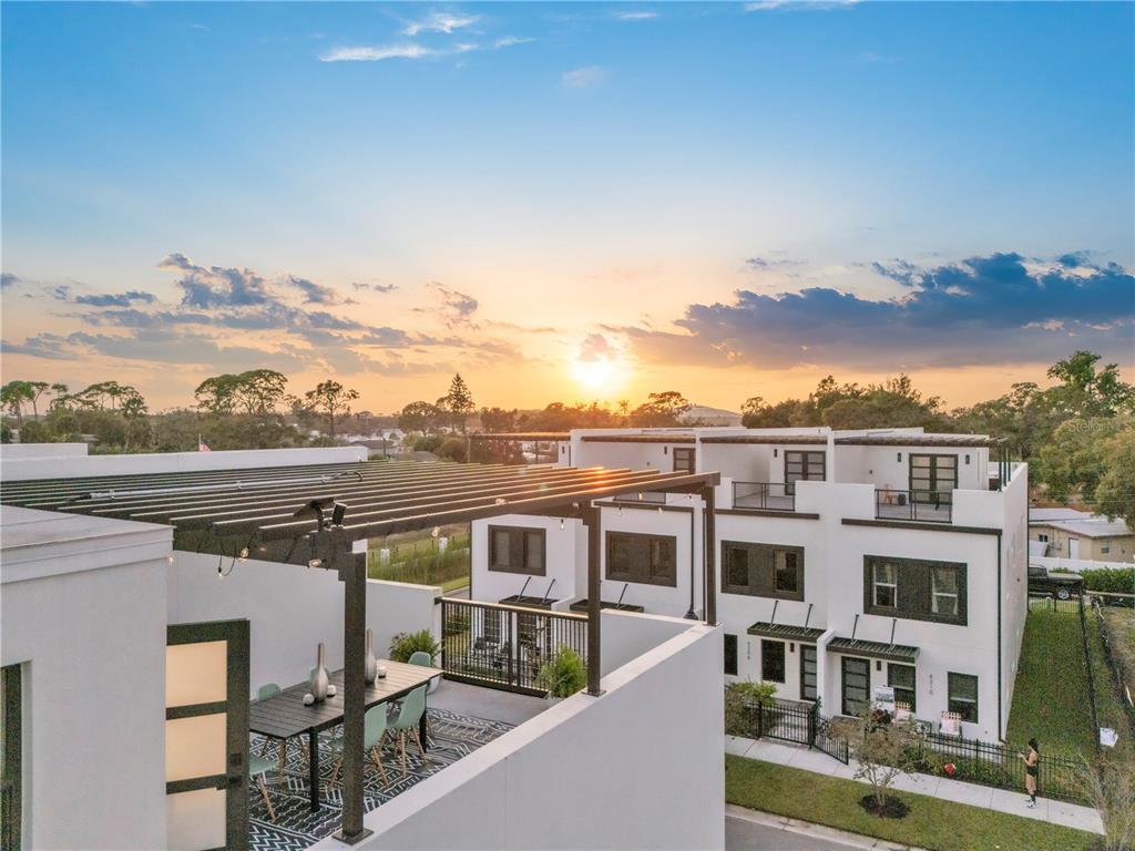 An elevated view of a modern white townhouse with a rooftop patio at sunset — 6207 64TH WAY N, PINELLAS PARK, FL
