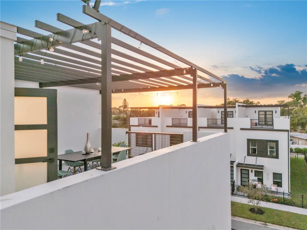 A modern rooftop terrace features a black metal pergola, string lights, and outdoor dining furniture — 6207 64TH WAY N, PINELLAS PARK, FL