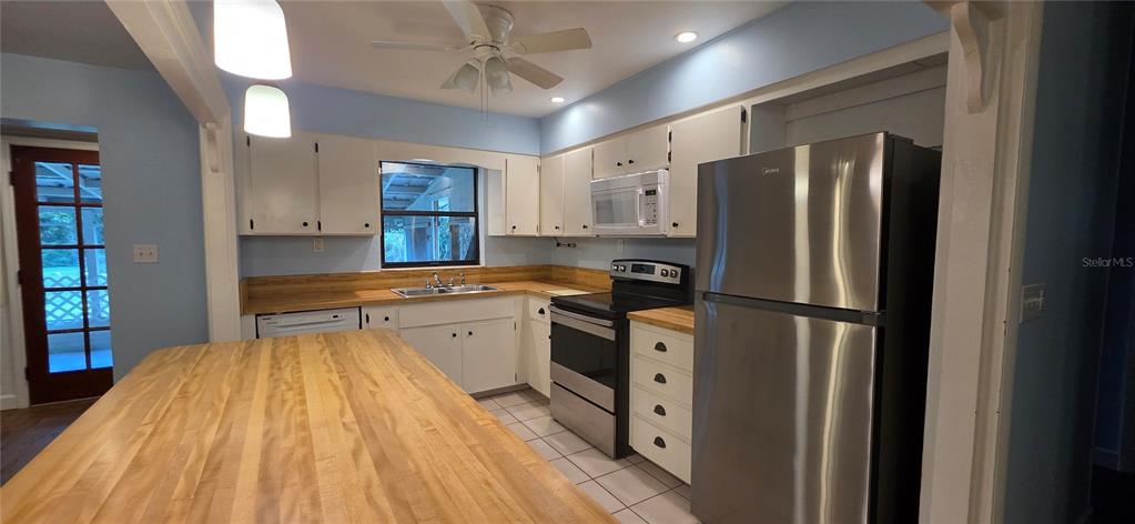 A kitchen features white cabinets, a wood countertop island, stainless steel appliances, and blue walls — 17451 SOUTHSIDE COURT, HIGH SPRINGS, FL